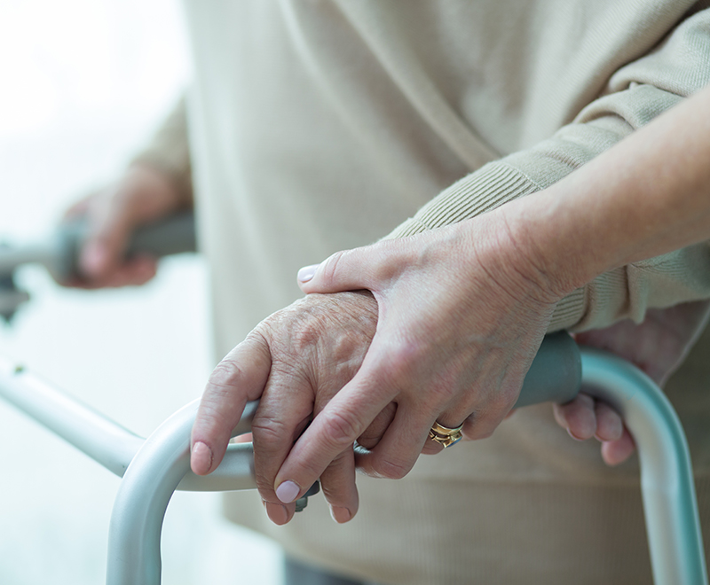 A caregiver helps an elderly patient use their walker.