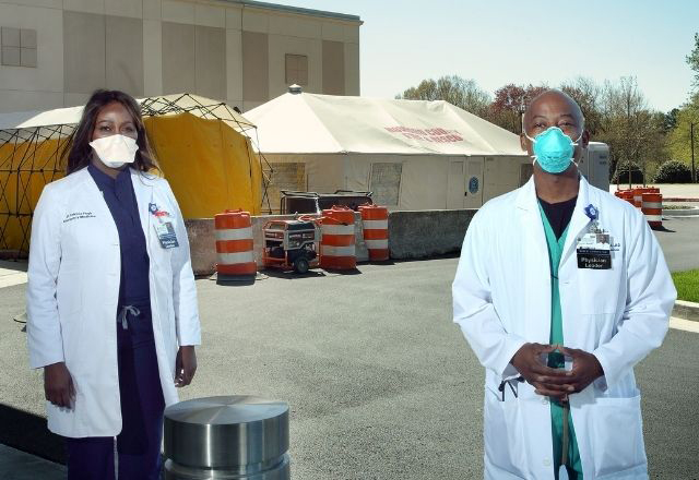Two Black Hopkins doctors wearing masks stand outside in front of a testing site.